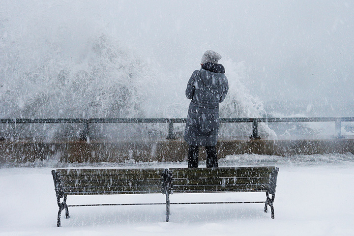 A woman watches as ocean waves crest the seawall in the Boston suburb of Lynn, Massachusetts, Jan.4, 2018.