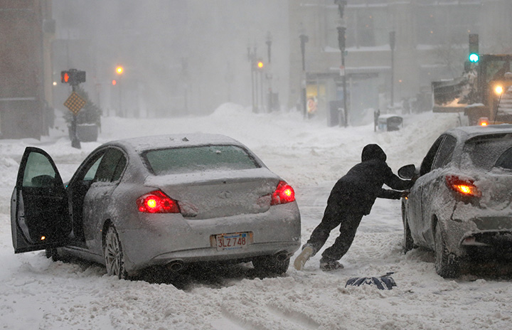 A motorist leaves his car to aid another stuck in downtown Boston during blizzard conditions on Jan. 04, 2018.