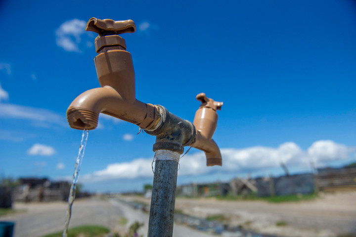 A communal tap runs as people collect water in an informal settlement near Cape Town, South Africa, Tuesday, Jan. 23, 2018. 