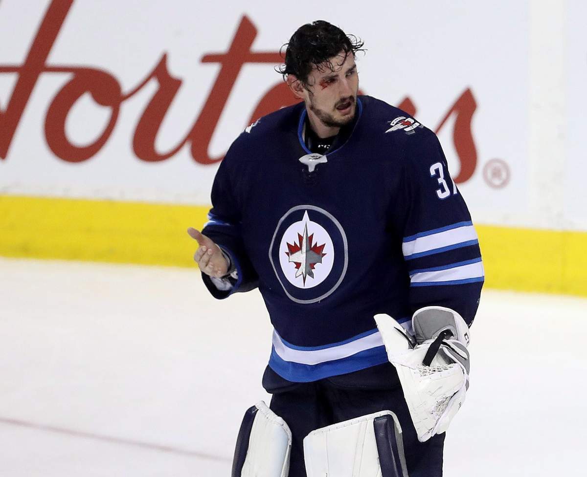 Winnipeg Jets goalie Connor Hellebuyck (37) reacts after getting a stick in the eye by Josh Morrissey (44) as he and Vancouver Canucks' Thomas Vanek (26) crashed into the net during third period NHL hockey action in Winnipeg, Sunday, January 21, 2018. THE CANADIAN PRESS/Trevor Hagan.