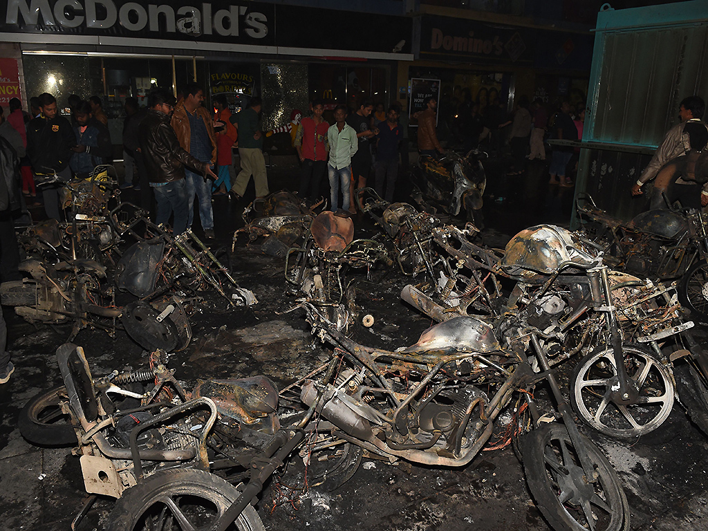 People walk around the charred remains of parked motorcycles, burned during protests against the film ‘Padmaavat,’ late on January 23, 2018 at the Himalaya Mall in Ahmedabad.