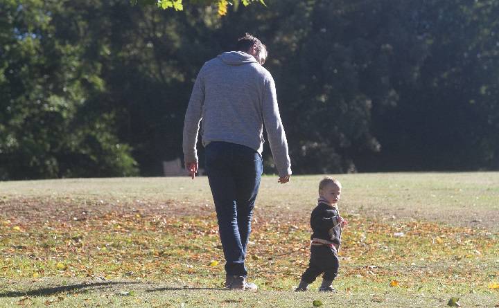 A father walks a toddler in the autumn sunshine.