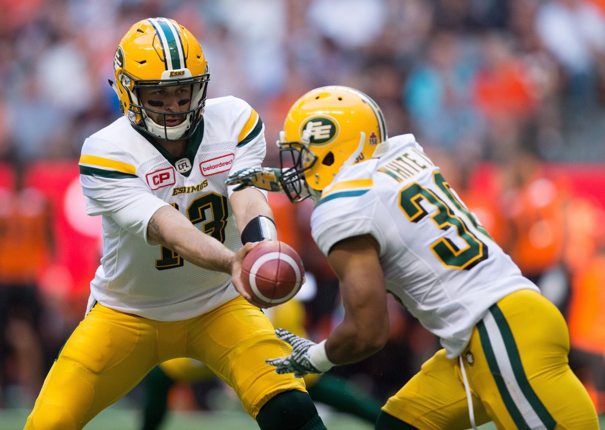 Edmonton Eskimos' quarterback Mike Reilly, left, hands off to John White during the first half of a CFL football game in Vancouver, B.C., on Saturday, June 24, 2017. 
