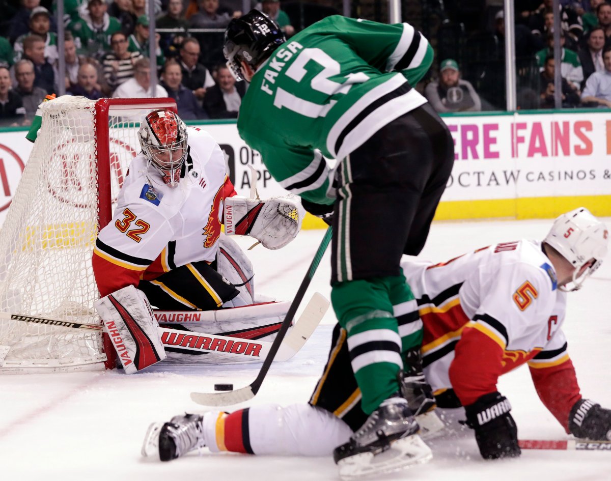 Calgary Flames goalie Jon Gillies (32) gets help from defenseman Mark Giordano (5) as Dallas Stars center Radek Faksa (12), of the Czech Republic, attacks the net during the first period of an NHL hockey game Tuesday, Feb. 27, 2018, in Dallas. (AP Photo/Tony Gutierrez).