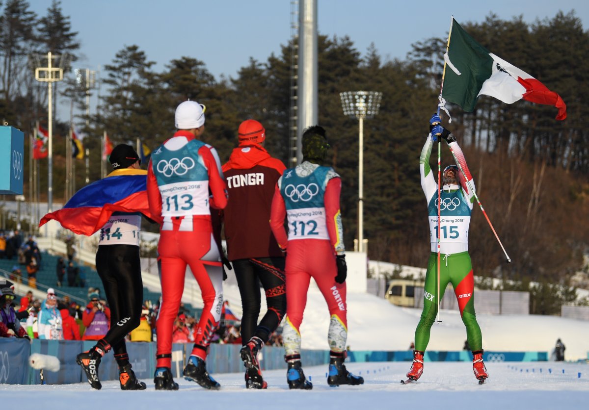 German Madrazo of Mexico holds his country's flag as he crosses the finish line, while Sebastian Uprimny of Colombia, Samir Azzimani of Morocco, Pita Taufatofua of Tonga and Kequyen Lam of Portugal look on during the cross-country skiing men's 15 km free on Feb. 16, 2018 in Pyeongchang, South Korea. 