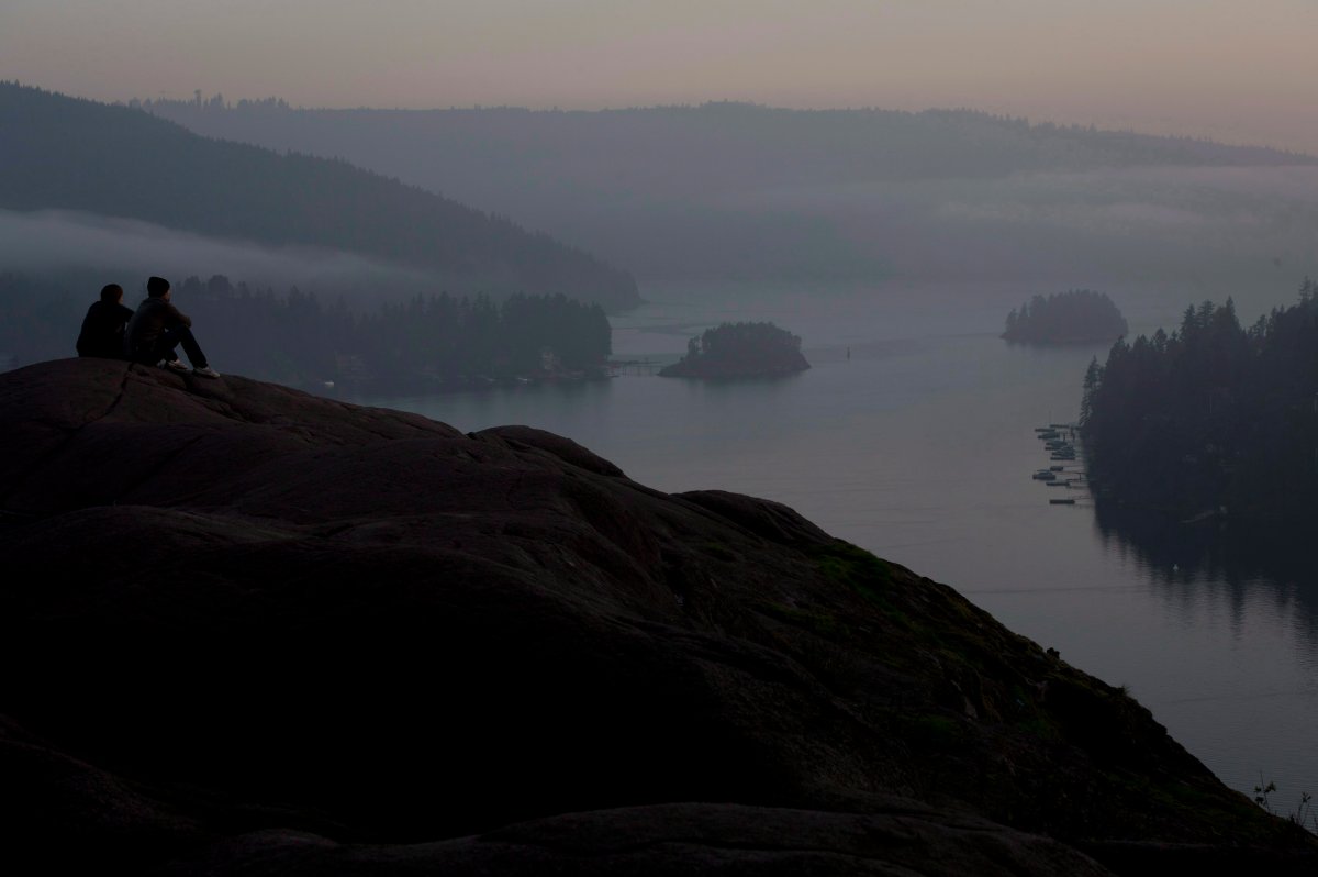 Hikers watch the setting sun through the fog atop of Quarry Rock at the end of the Baden Powel trail in Deep Cove in North Vancouver, B.C., on Monday, Oct. 21, 2013. 