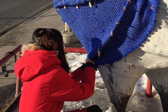 ACAD student Yilu Xing making alterations on the sweater made for the chicken statue outside of Chicken on the Way in Kensington.