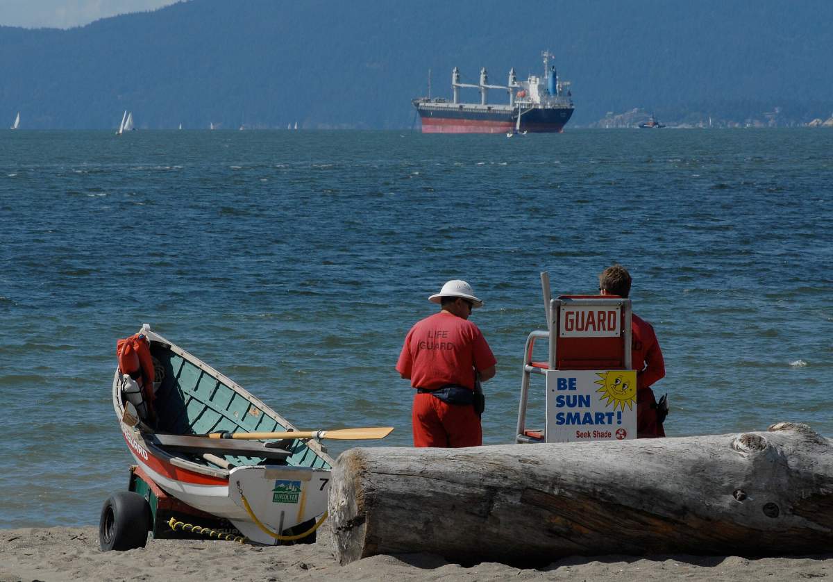 Lifeguards stand next to a rescue boat as they look over English Bay beach in Vancouver, British Columbia, Canada.