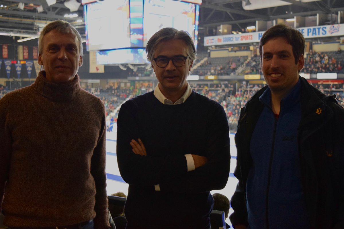 Swiss curling fans Manuel Noseda (left) and Mauro Frigerio (right) pose with the president of their curling club in front of four bustling sheets of ice during draw 11 at the Tim Hortons Brier in Regina, Sask.
