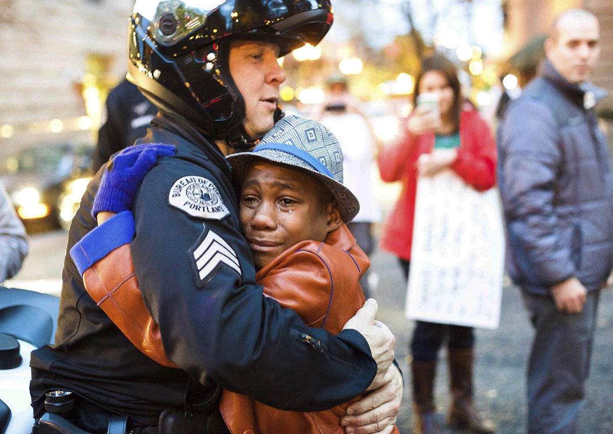 In this Nov. 25, 2014, file photo provided by Johnny Nguyen, Portland police Sgt. Bret Barnum, left, and Devonte Hart, 12, hug at a rally in Portland, Ore., where people had gathered in support of the protests in Ferguson, Mo. 