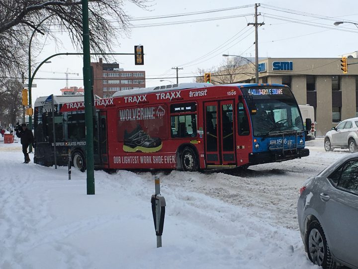 A city transit bus is hung up in snow on a downtown street.