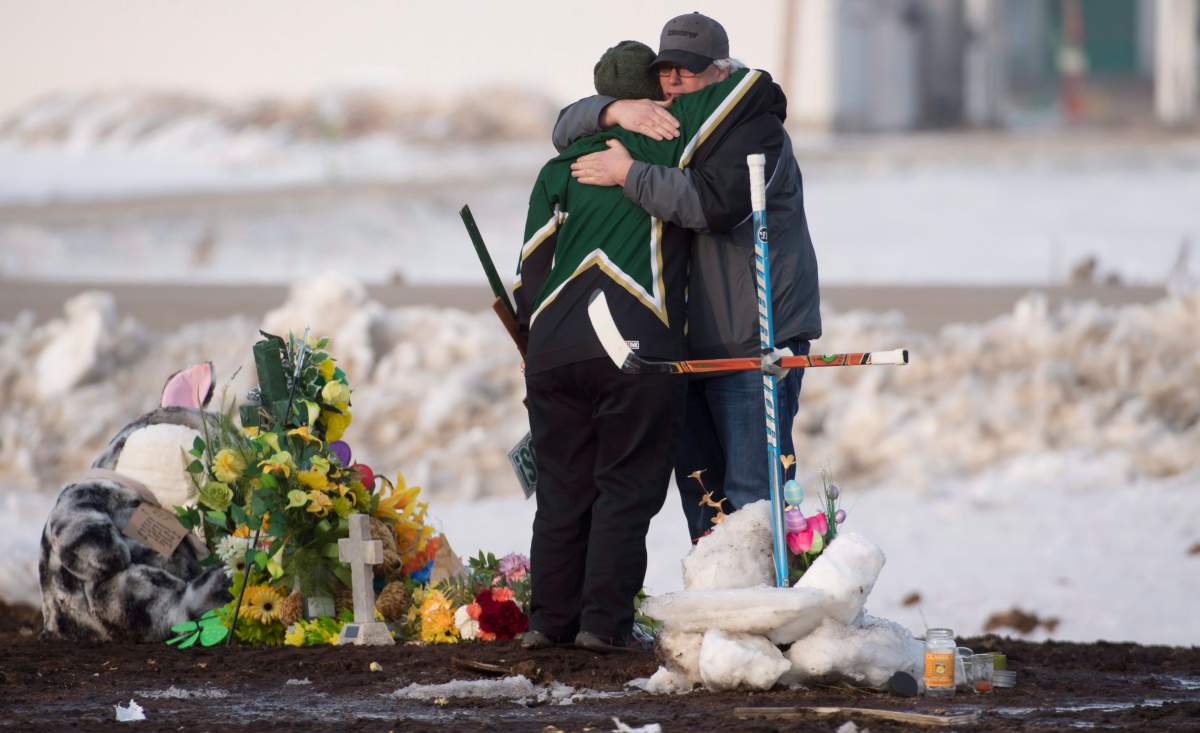 People hug and pay their respects at a makeshift memorial at the intersection of a fatal bus crash near Tisdale, Sask., on Monday, April, 9, 2018. A bus carrying the Humboldt Broncos hockey team crashed into a truck en route to Nipawin for a game Friday night killing 15 and sending over a dozen more to the hospital.