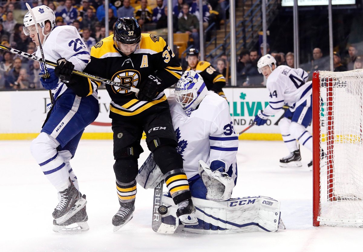Toronto Maple Leafs goaltender Curtis McElhinney makes a save as Boston Bruins' Patrice Bergeron and defenseman Travis Dermott battle for position during the second period of Game 2 of an NHL hockey first-round playoff series in Boston, Saturday, April 14, 2018.