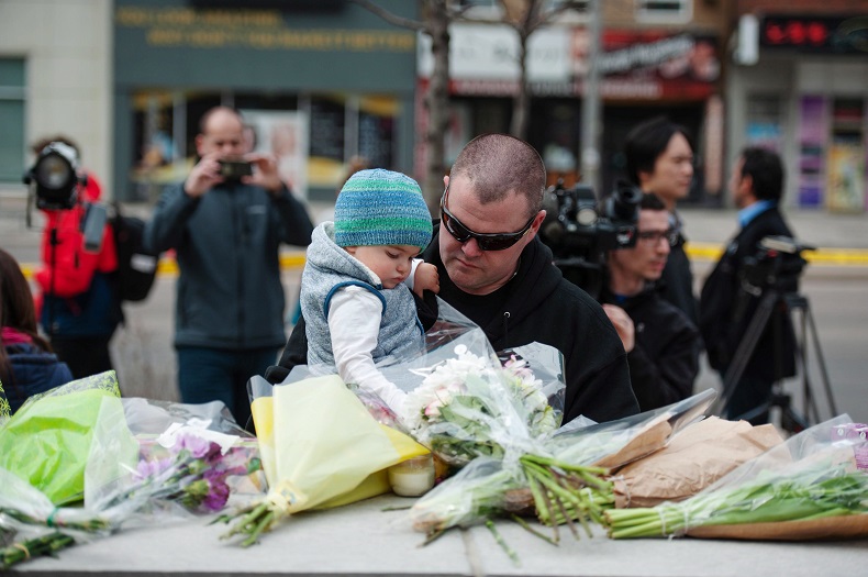 Sean O'Keefe and his son Fionn, 16 months, bring flowers to a memorial on Yonge Street the day after a driver drove a rented van down sidewalks Monday afternoon, striking pedestrians in his path in Toronto, Tuesday, April 24, 2018. 