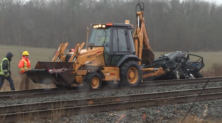 A car is pulled from the side of railway tracks after it was destroyed by a passenger train. The three men involved in the crash have been charged by Kingston police.