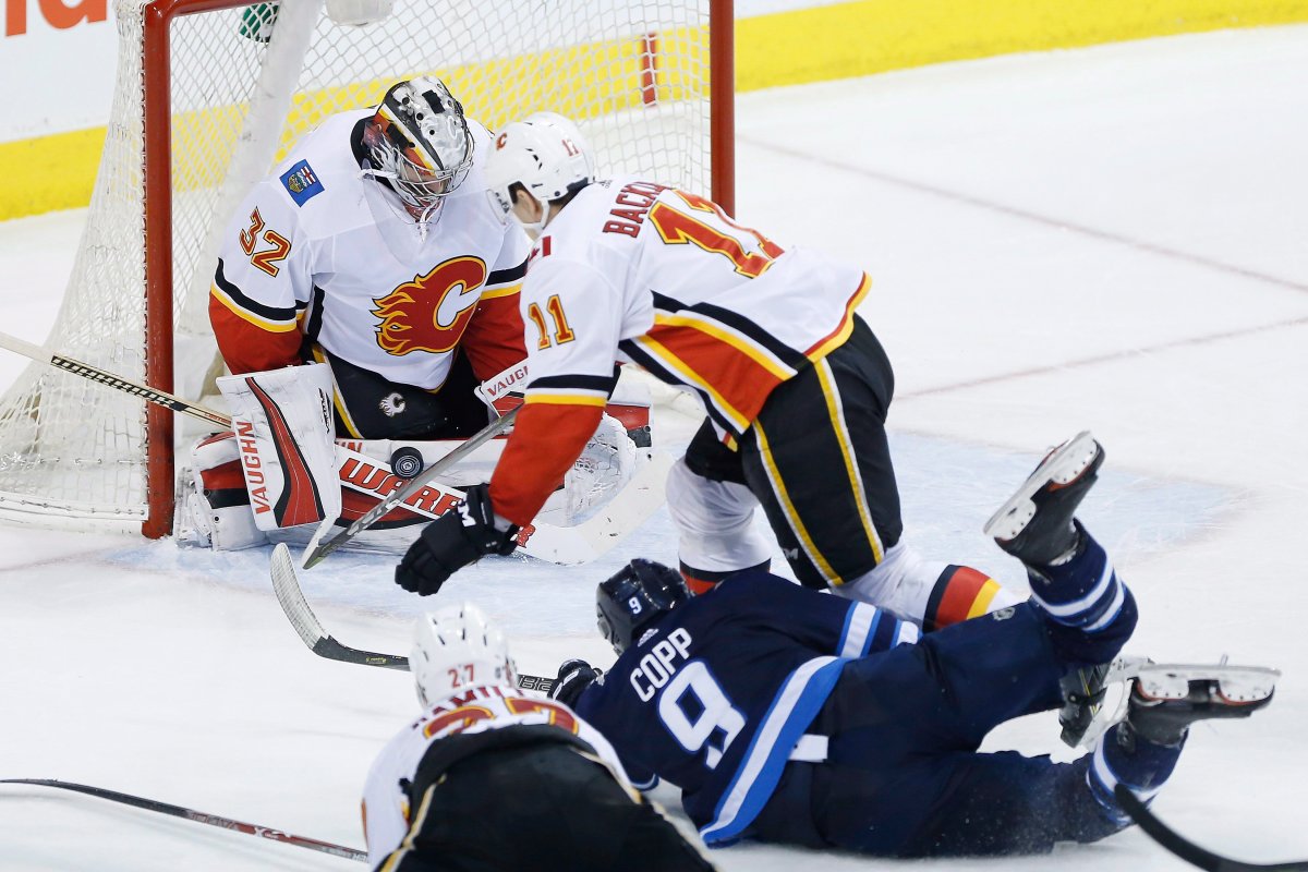 Calgary Flames goaltender Jon Gillies (32) saves the shot by Winnipeg Jets' Andrew Copp (9) as Mikael Backlund (11) defends during third period NHL action in Winnipeg on Thursday, April 5, 2018. THE CANADIAN PRESS/John Woods.