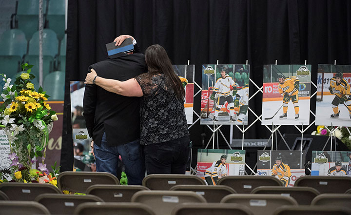 A man is comforted as he looks at photographs before a vigil at the Elgar Petersen Arena, home of the Humboldt Broncos, to honour the victims of a fatal bus accident, April 8, 2018.