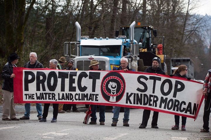 Protesters hold a banner as a transport truck attempting to deliver heavy equipment to Kinder Morgan sits idle as others block a gate at the company's property in Burnaby, B.C., on Monday, March 19, 2018. The federally approved Kinder Morgan pipeline expansion has been put on hold due to opposition.