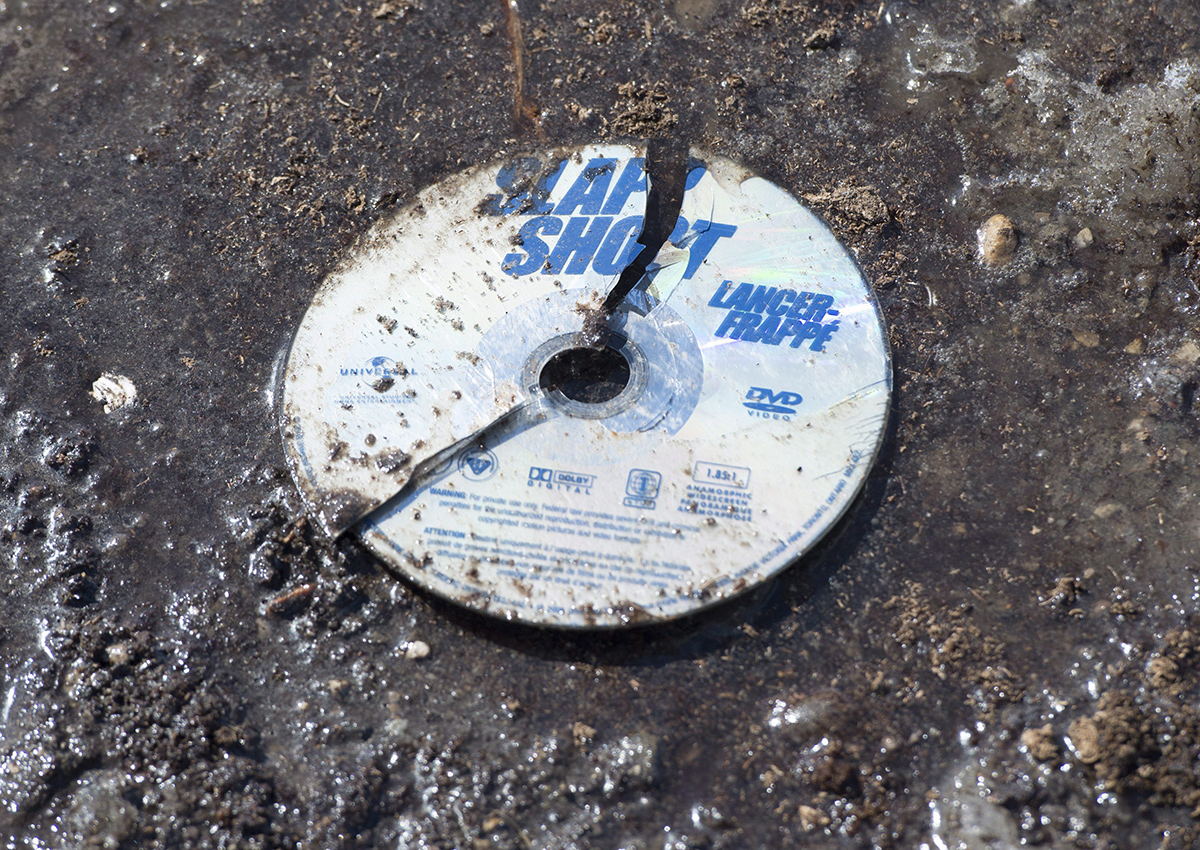 A broken DVD of the hockey movie Slap Shot is seen in the mud at the intersection of a crash site near Tisdale, Sask., Sunday, April 8, 2018. 
