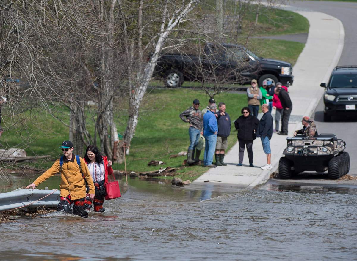 Simon Barton, left, and Chelsea Burley wear make shift waders of garbage bags and packing tape as they cross a flooded road in Saint John, N.B. on Sunday, May 6, 2018. Swollen rivers across New Brunswick are still rising, flooding streets and properties and forcing people from their homes in several communities.