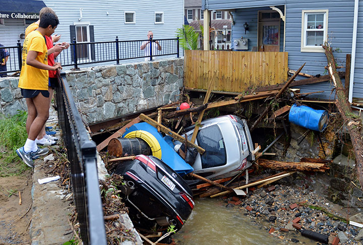 Residents gather by a bridge to look at cars left crumpled in one of the tributaries of the Patapsco River that burst its banks as it channeled through historic Main Street in Ellicott City, Md., Monday, May 28, 2018.