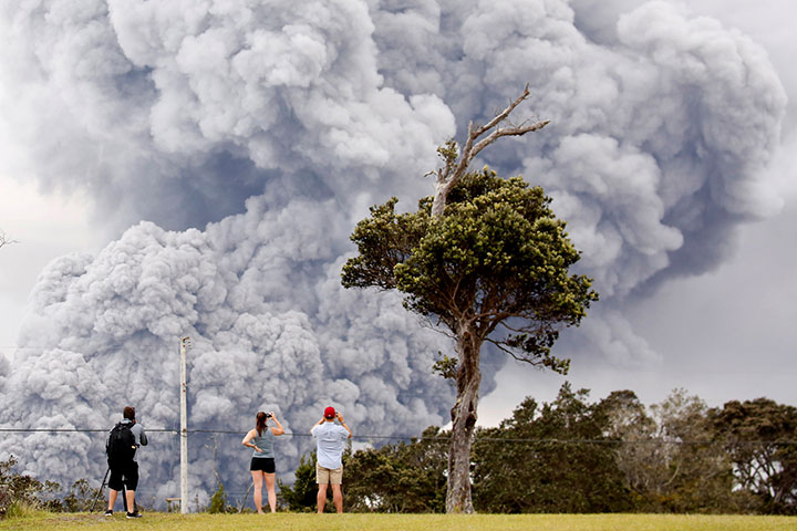 People watch as ash erupts from the Halemaumau crater during ongoing eruptions of the Kilauea Volcano in Hawaii, May 15, 2018.