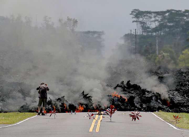 In this May 5, 2018 file photo, offerings of ti leaves, rocks and cans to the fire goddess Pele, lie in front of lava as it burns across a road in the Leilani Estates subdivision as a man takes pictures of the flow near Pahoa, Hawaii.