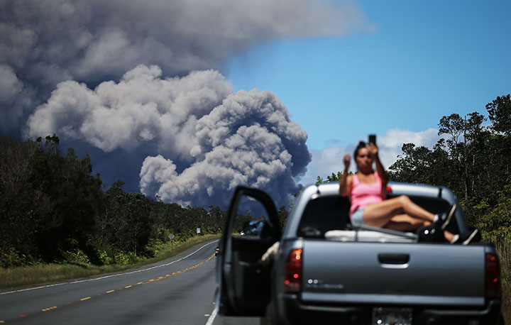 A woman takes a photo as an ash plume rises from the Kilauea volcano on Hawaii’s Big Island on May 15, 2018.