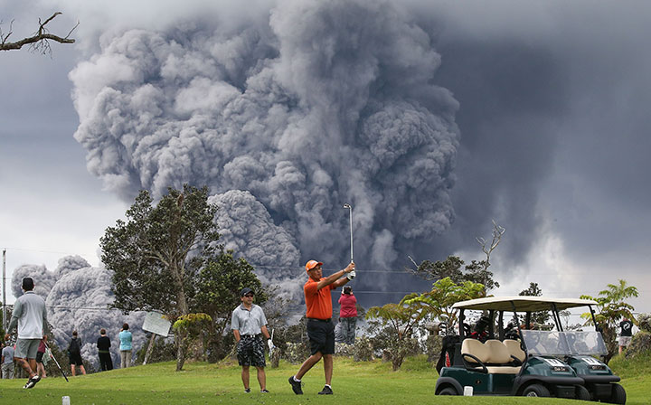 People play golf as an ash plume rises in the distance from the Kilauea volcano on Hawaii’s Big Island on May 15, 2018 in Hawaii Volcanoes National Park.