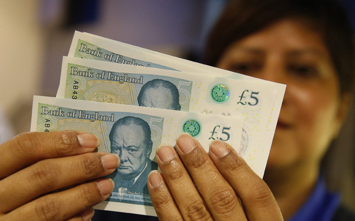 A member of staff at a branch of Halifax bank, in London, displays the British 5-pound sterling notes.