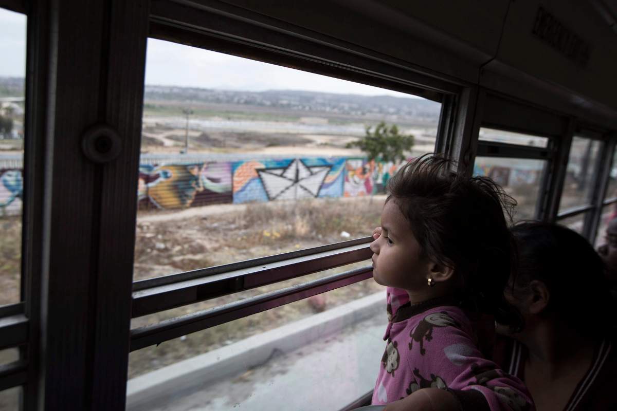A Central American child peers at the border wall from a bus carrying migrants to Tijuana, Mexico on Sunday, April 29, 2018. (AP Photo/Hans-Maximo Musielik)