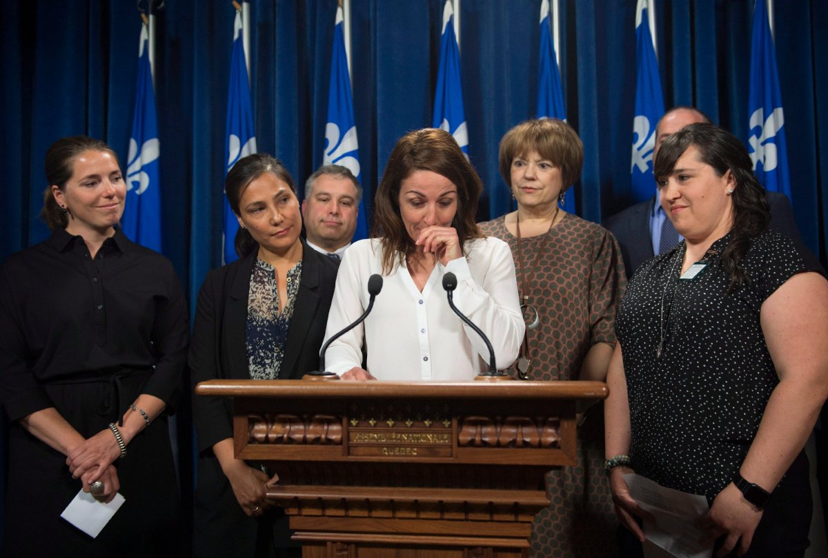 Former National ski team member Gail Kelly, centre, reads a statement over the Quebec government's measures to prevent sexual assault against athletes as Genevieve Simard, from left, Anna Prchal, and Emilie Cousineau, right, look on at a news conference, Tuesday, June 12, 2018 at the legislature in Quebec City. Quebec Education and Family Minister Sebastien Proulx, third left, and Minister responsible for Higher Education and Minister responsible for the Status of Women Helene David, second right, stand at their side. 