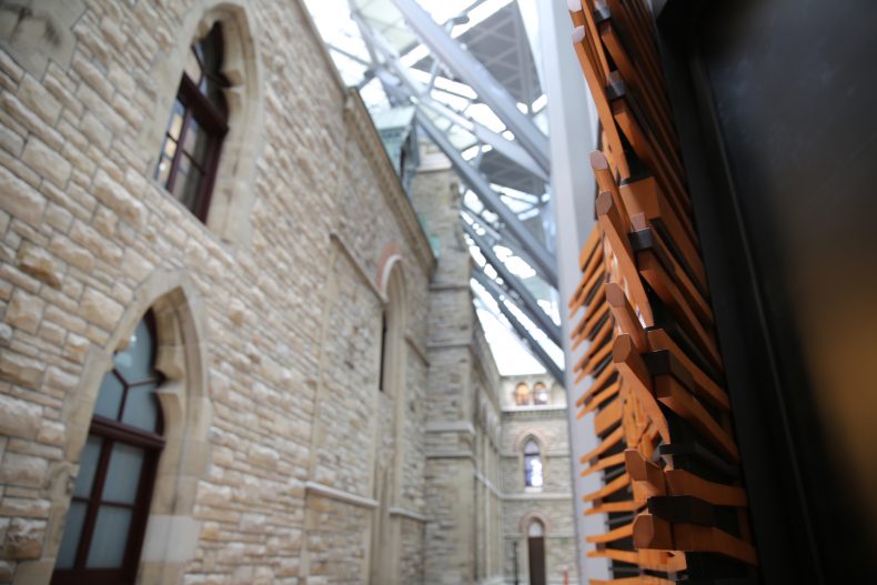 The antechamber of the new House of Commons showcases the intersection of the two structures. In the foreground, there is an example of the wood finishes meant to enhance the acoustics of the space.