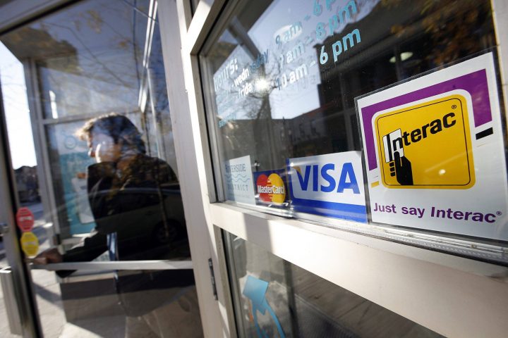 Toronto, Nov. 11/09 - A person exits a store on Queen Street East in Toronto, Ontario, Canada, with an Interac sign as well as Visa and MasterCard signs.