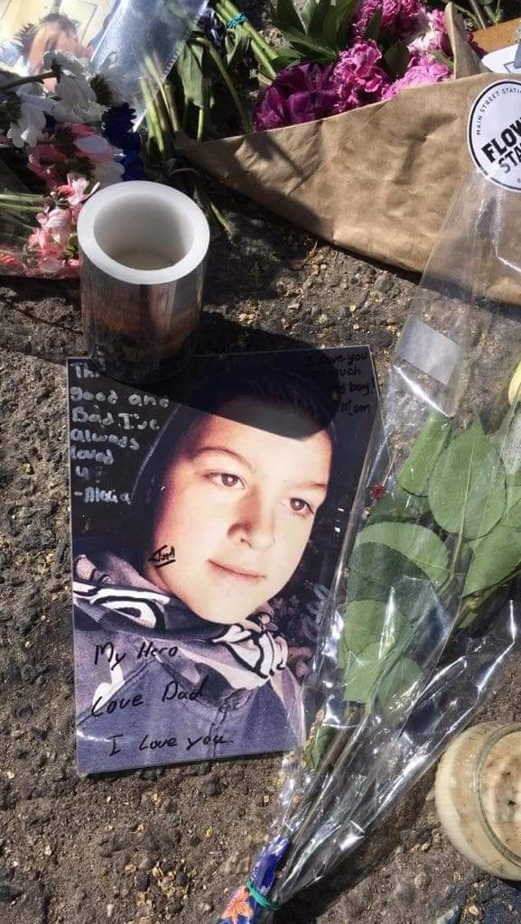 A photo of Athan McEwen lies beneath a candle. A message from his father reads “My hero, Love Dad”