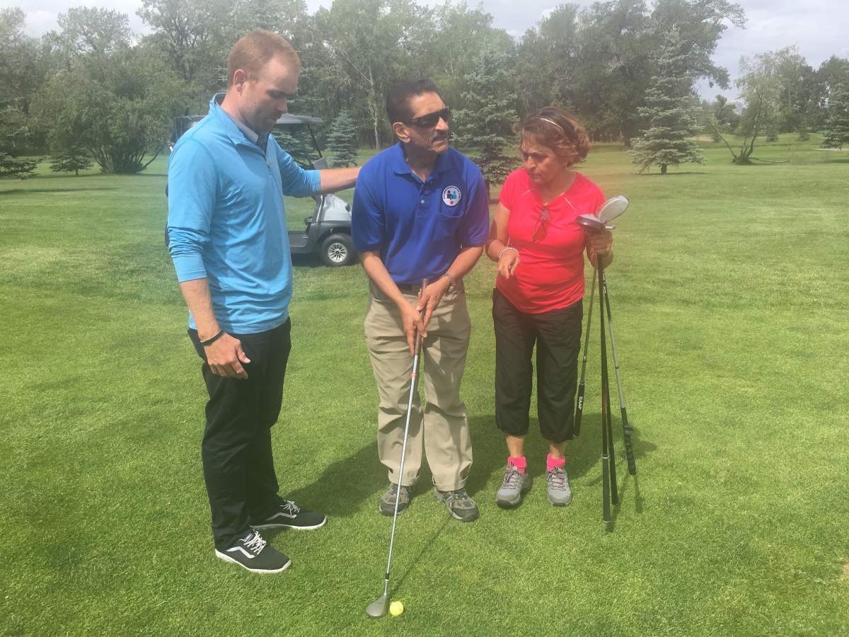 Golfer Shabu Hussein, who is blind, gets help from his wife Shaida and instructor Scott Stiles at Inglewood Golf Club in Calgary on June 28, 2018.