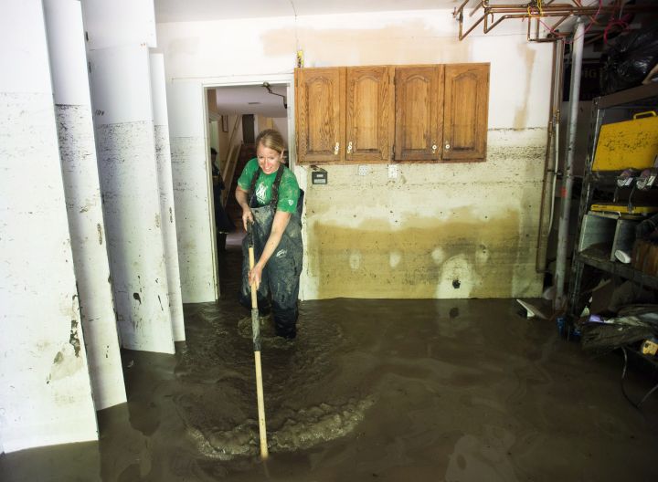 Sarah Watts sweeps out water from the house to the garage with hip waiters on as they try to pump the water out in the community of Bowness in Calgary, Alta., on Monday, June 24, 2013.