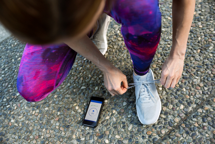 FILE - Runner tying shoe and checking heart rate app on cell phone
.