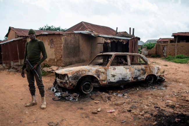 A member of the security forces stands next to a burnt out vehicle in the Nghar Village, near Jos on June 27, 2018, after Fulani herdsmen attacked the village. 


