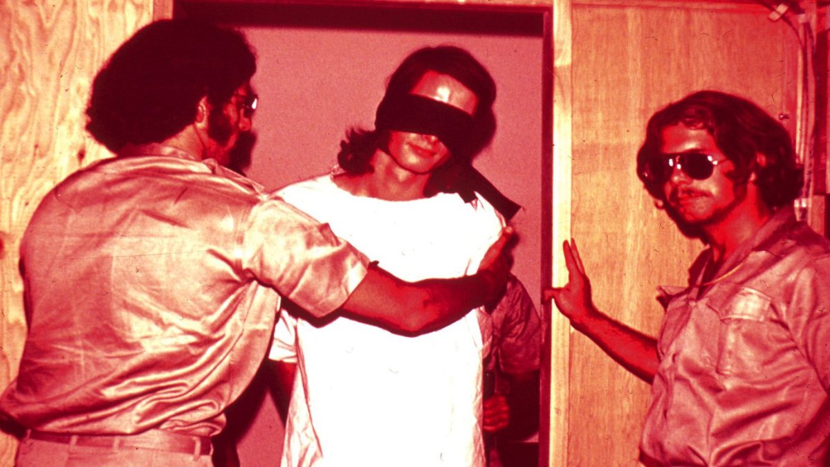 Two guards stand with a blindfolded prisoner in this image from the 1971 Stanford Prison Experiment.