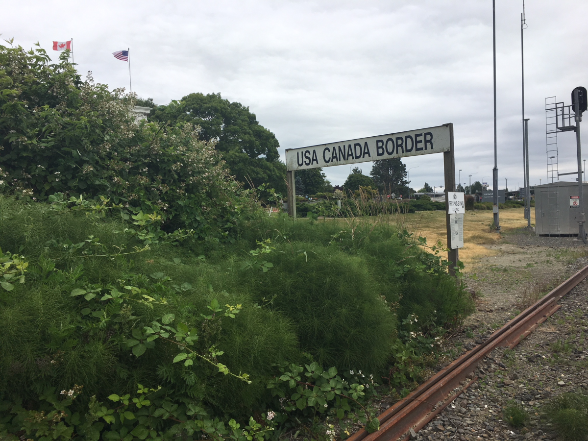 A sign near some bushes denoting the U.S.-Canada border in White Rock.