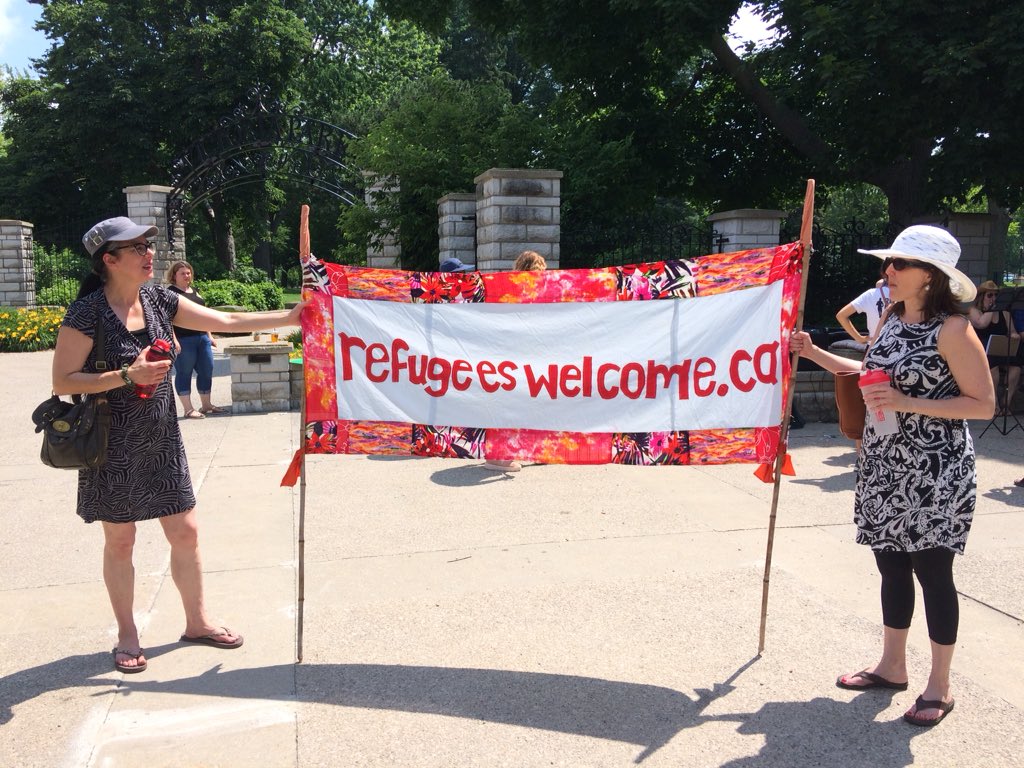 Two marchers hold up a sign, welcoming refugees and migrants to Canada. 