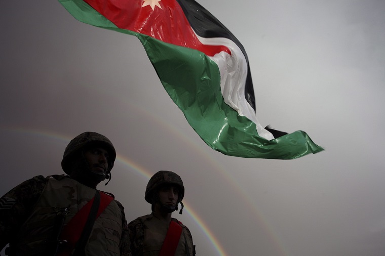Jordanian border soldiers stand below a Jordanian national flag as the rainbow appears, prior to the arrival of Syrian refugees who will  be crossing into Ruweishid, Jordan, Thursday, Dec. 5, 2013. 
