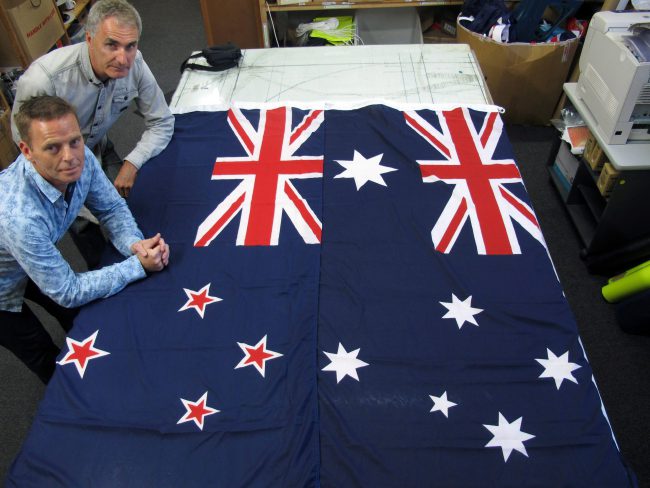 Managers at flag manufacturer Flagmakers pose next to flags of New Zealand, left, and Australia, in their factory near Wellington, New Zealand, March 3, 2014.