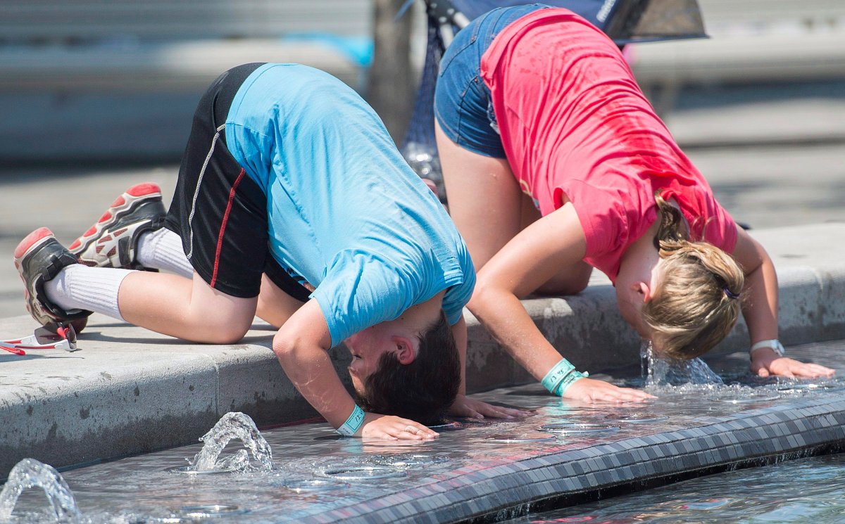A boy and girl dunk their heads in a water fountain during a heatwave in Montreal, Monday, July 2, 2018. 