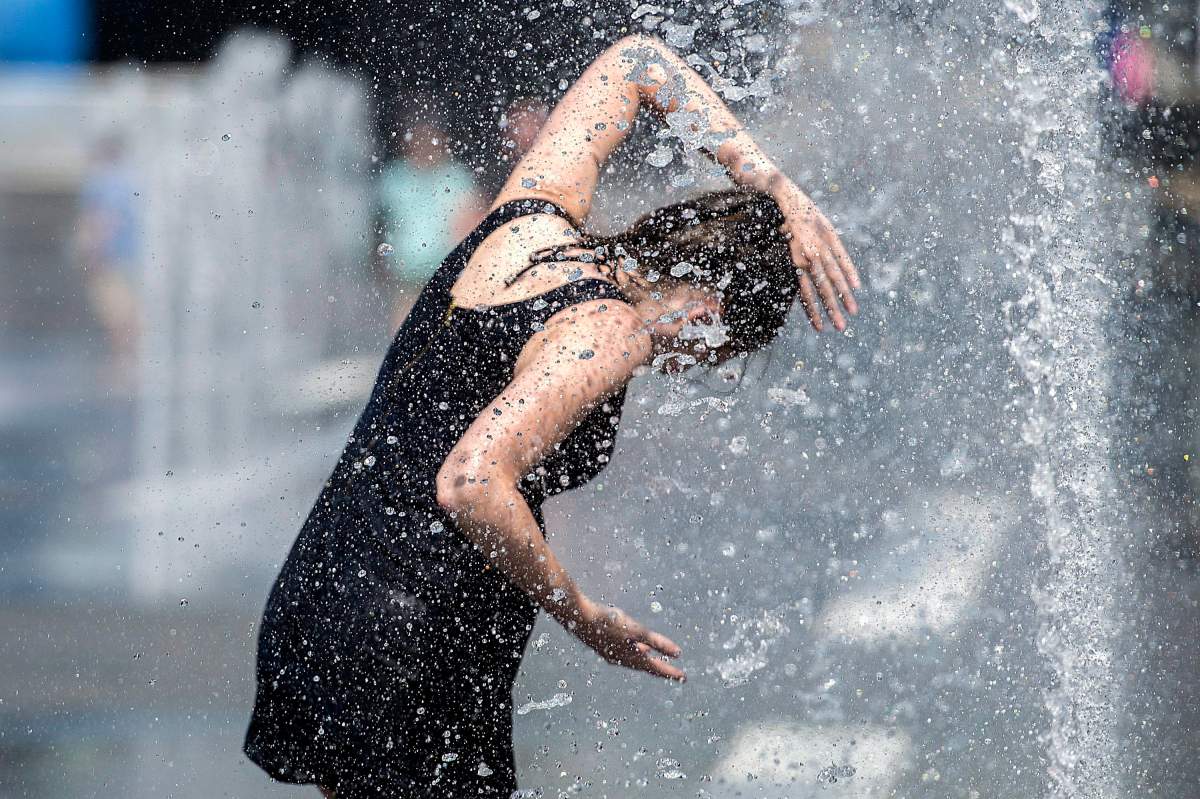 A woman cools down in a water fountain as she beats the heat in Montreal, Monday, July 2, 2018.