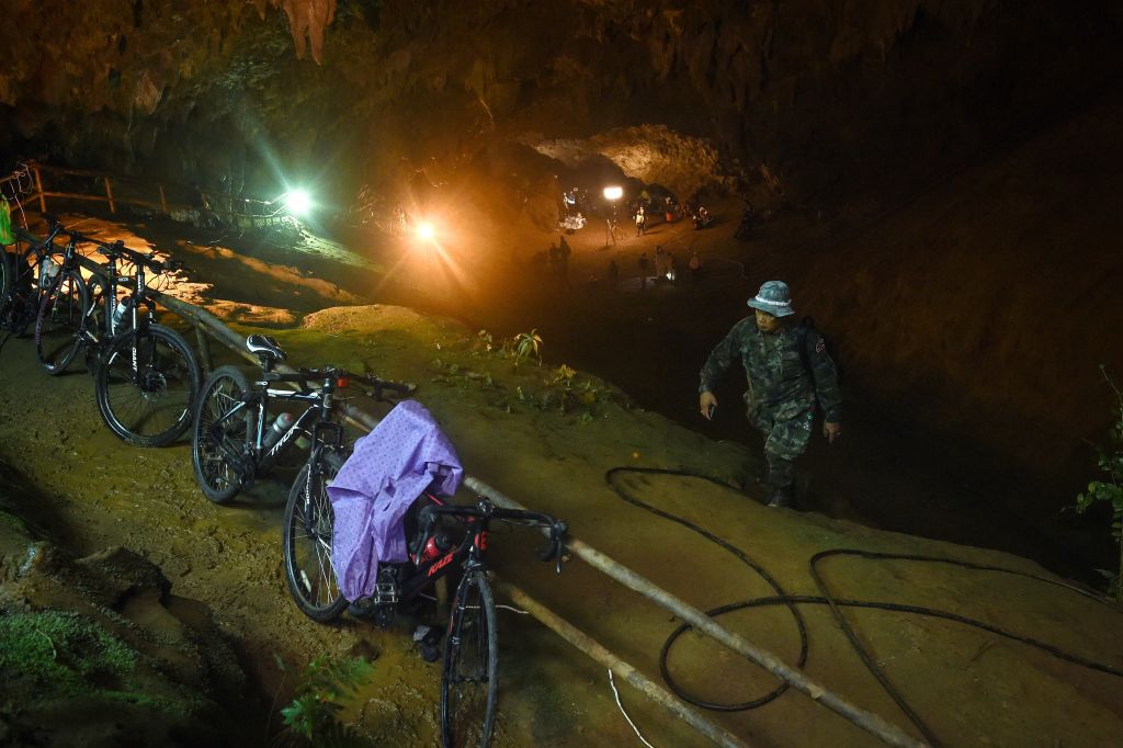 The abandoned bicycles belonging to the missing children are seen parked together while Thai rescue personnel conduct rescue operations under floodlights, seen in the background, at the entrance of Tham Luang cave in Chiang Rai province on June 26, 2018 as the search continue for the 12 children and their coach.