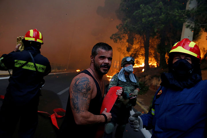 Firefighters, soldiers and local residents carry a hose as a wildfire burns in the town of Rafina, near Athens, Greece, July 23, 2018.