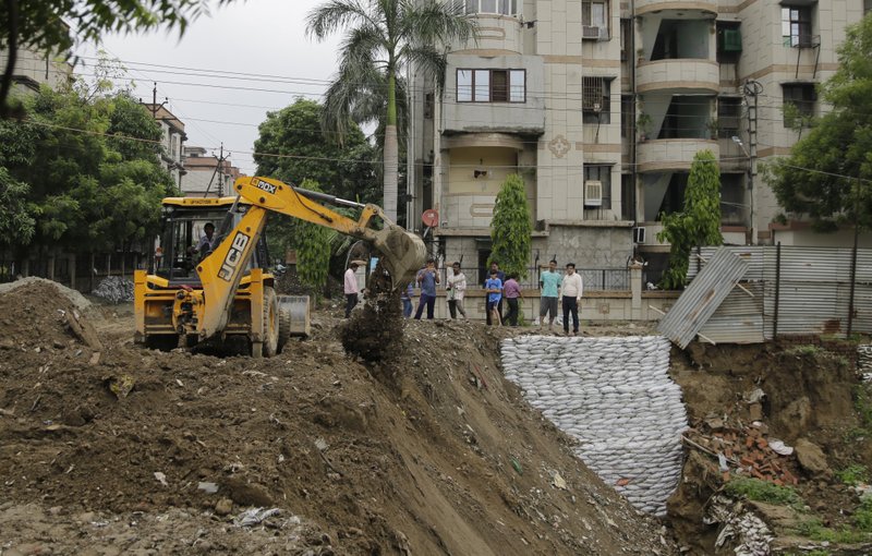 Residents watch as an earthmover fills up a road which caved in during heavy rainfall near Ghaziabad, in the northern Indian state of Uttar Pradesh, Saturday.