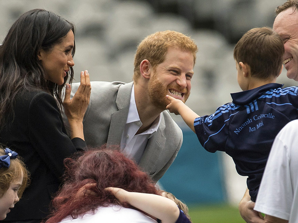 A boy strokes Prince Harry’s beard, as Meghan, the Duchess of Sussex, smiles on the pitch at Croke Park on July 11, 2018.
